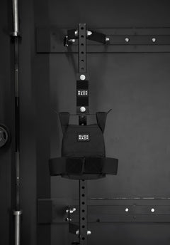 A Ruck Rack® Monster, a versatile mount for rucks, weight vests, and tactical gear, is mounted on a metal storage rack in the gym alongside a barbell—showcasing a sturdy organizer ideal for American-made gear storage.