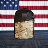 GORUCK rucksack with camouflage front panel on table, US flag background, tough rucking gear