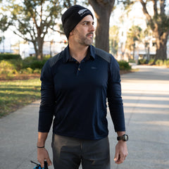 A man stands outdoors on a sunny day, wearing the Men's Long Sleeve Rucking Polo and a black beanie, looking to the side.