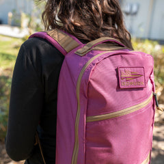 A person wearing the Bullet Ruck Classic - Ballistic Nylon Cordura 15L daypack in magenta is outdoors, seen from behind with greenery in the background.