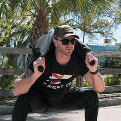 Man outdoors squats with a Bulgarian Sandbag, gripping its reinforced handles and balancing the crescent-shaped sandbag over his shoulders.