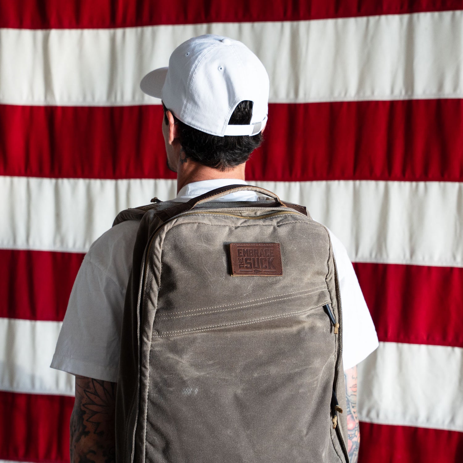 Wearing a white cap and shirt, a person with a large backpack featuring the 
