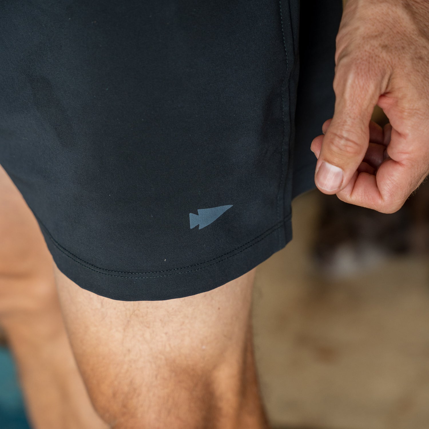 A person’s hand next to Men’s Training Shorts - ToughStretch in black, featuring a small arrowhead logo near the hem.