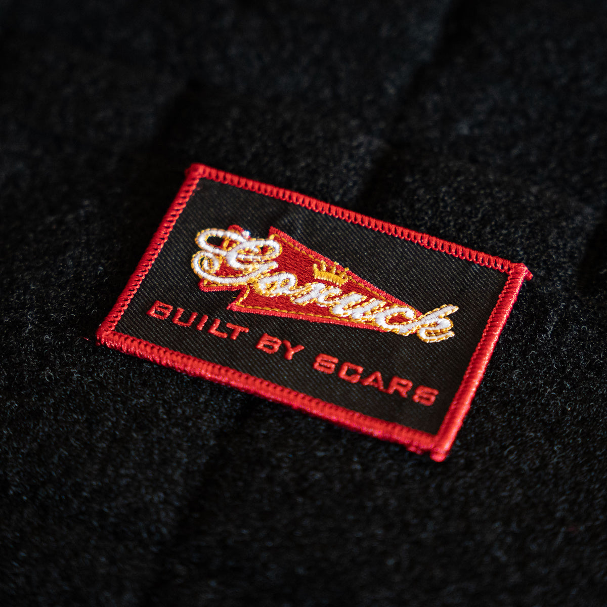 The Scrap Shooter is a black fabric patch with a red border, featuring 