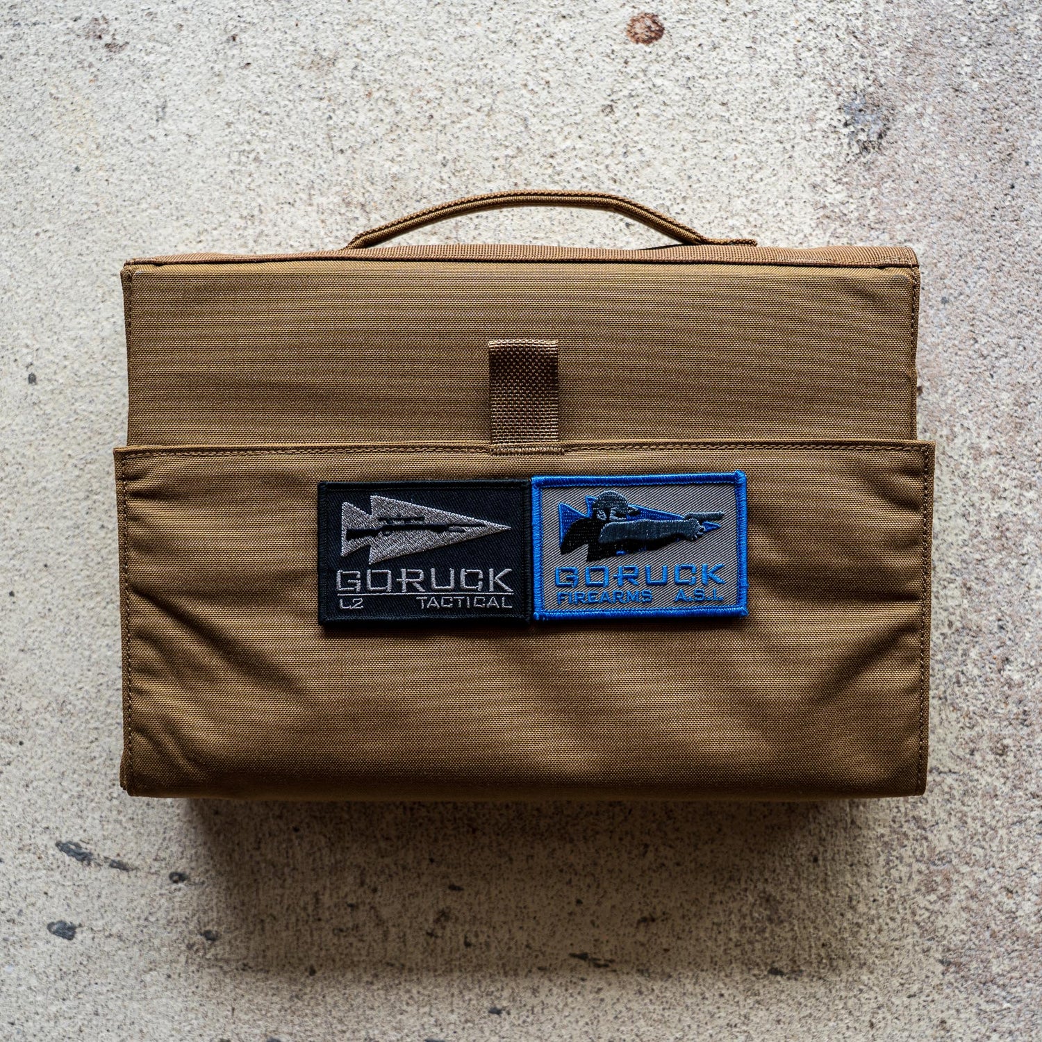 The Ammo Book is a brown tactical bag with two GORUCK patches, designed for ammo storage and shown on a textured, light-colored surface.