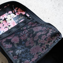 Midnight Blossum Waxed Bullet - Built by Scars displayed open, revealing a pink floral interior with a mesh pocket and custom stitching, set on a light textured surface.