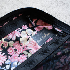 Close-up of the Midnight Blossum Waxed Bullet - Built by Scars, a zippered bag crafted from heritage waxed canvas with a floral interior and a visible GORUCK label inside.