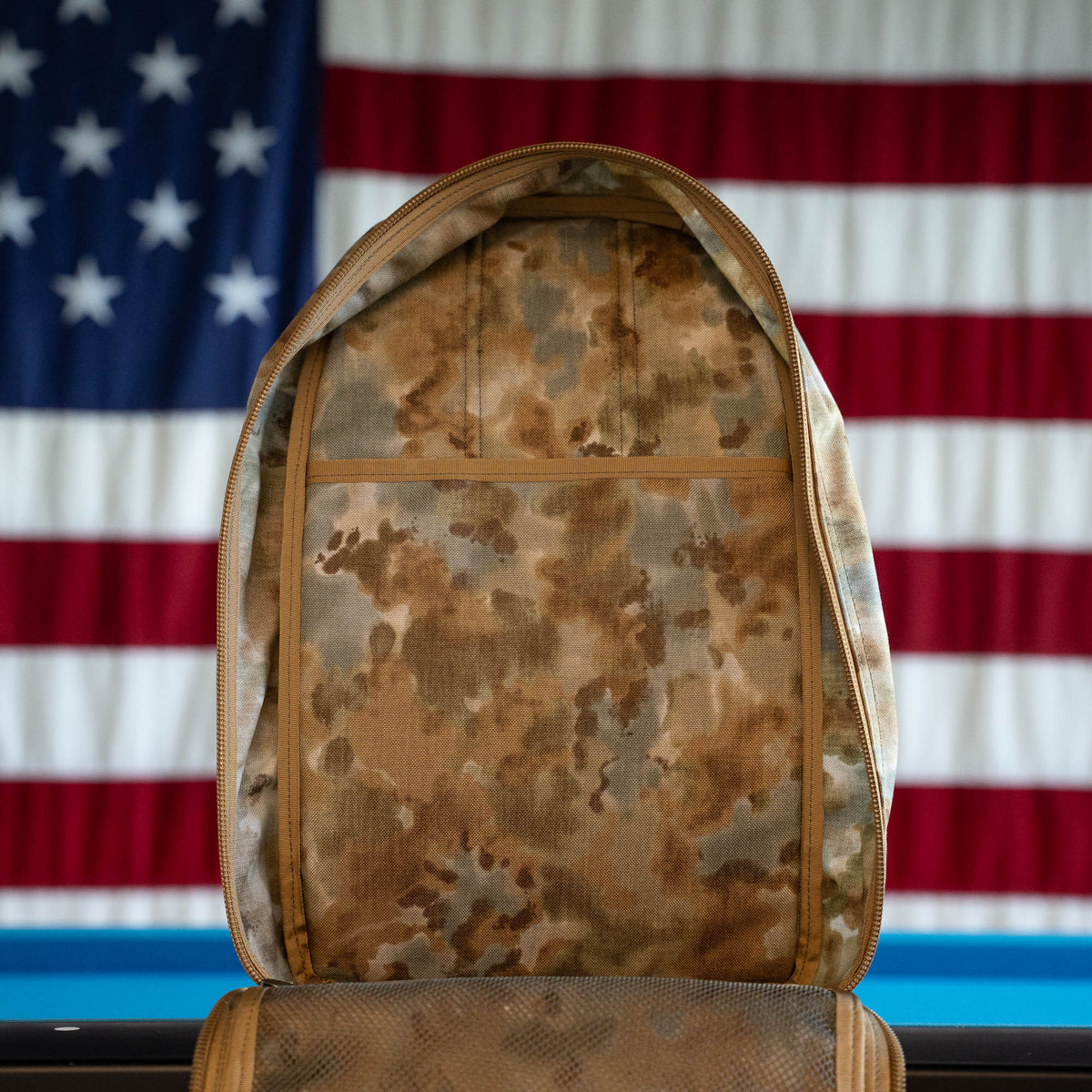 Arid Bullet - Built by Scars: This limited edition camouflage backpack is a handmade ruck, open in front of an American flag backdrop and crafted with care in Jax Beach, Florida.