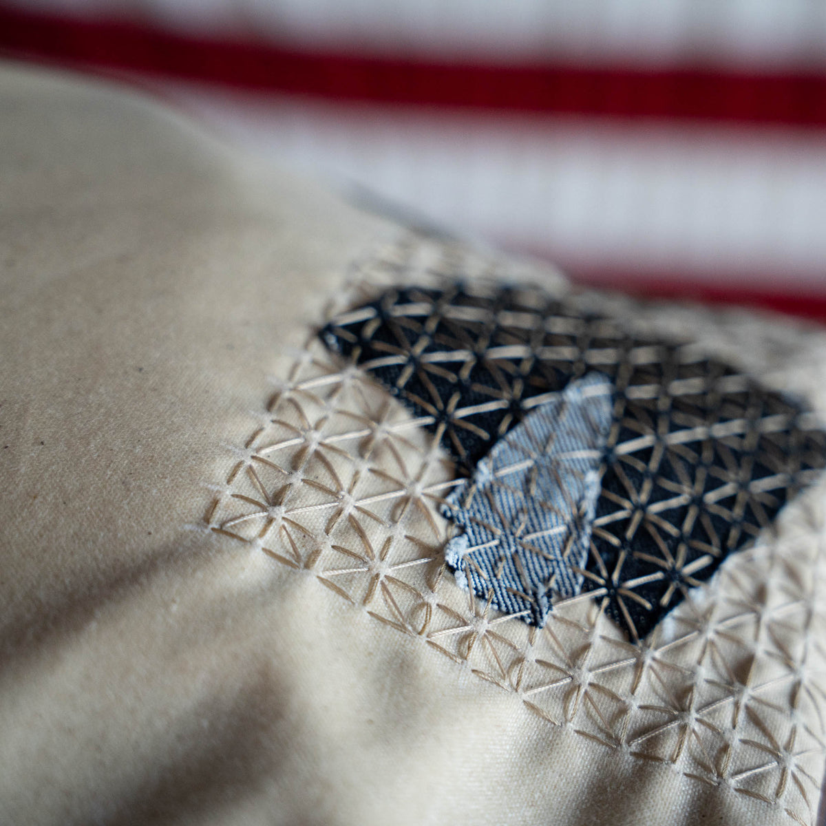 Close-up of beige fabric with geometric embroidery in dark and light threads, background blurred. The Waxed Bullet is a limited edition piece, handmade as part of a ruck collection inspired by the coastal charm of Jax Beach, Florida.