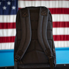 A Checkered GR1 21L - Built by Scars backpack with padded straps and unique designs sits in front of an American flag background.