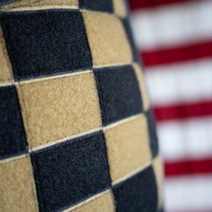 Close-up of the Checkered GR1 21L - Built by Scars, featuring a black and tan checkerboard pattern with red and white stripes blurred in the background; this limited edition, handmade ruck is inspired by Jax Beach, Florida.