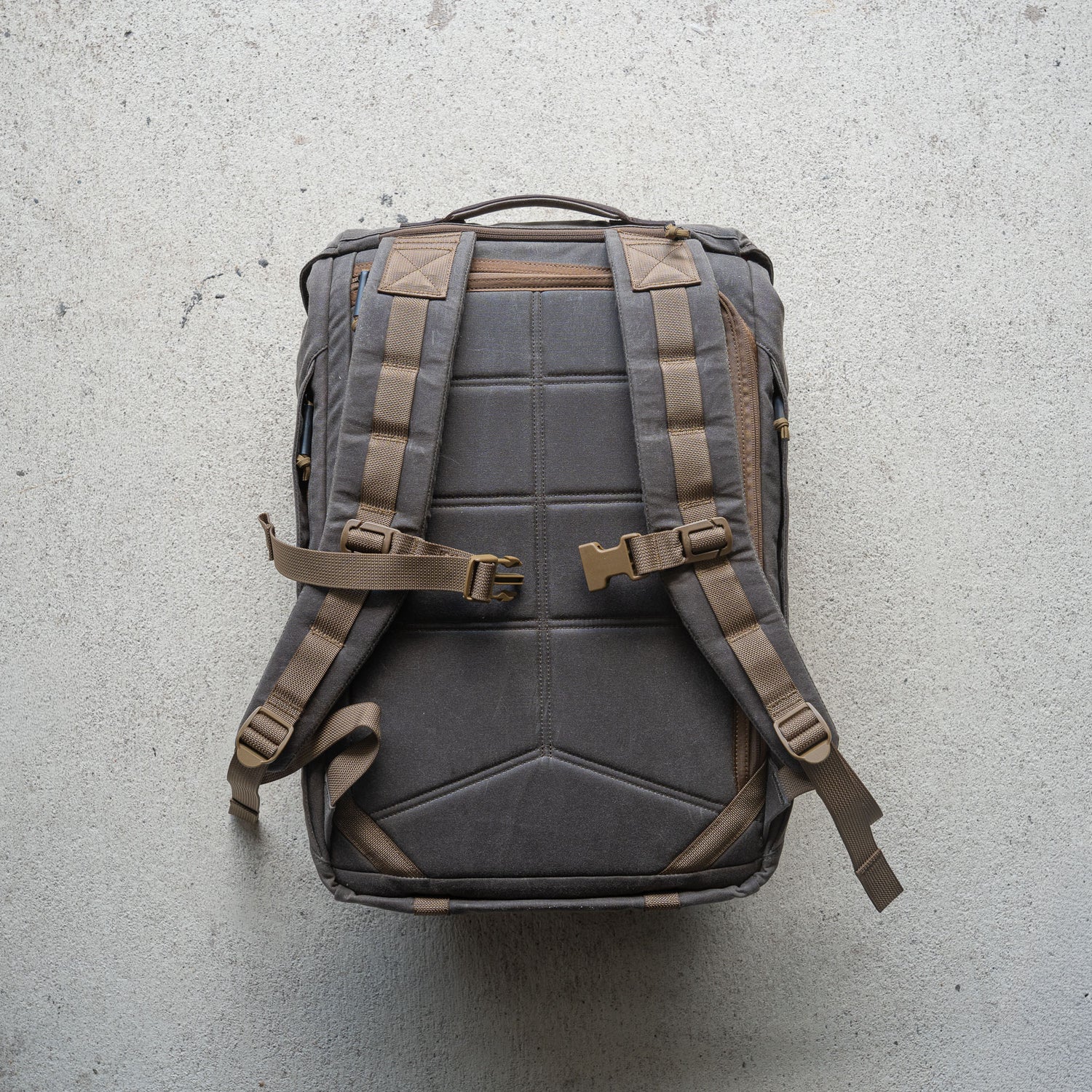 The M26 PREORDER // Q4 2026 ETA backpack, featuring padded straps, buckles, and a bombproof laptop compartment, is displayed flat on a textured light-colored surface.