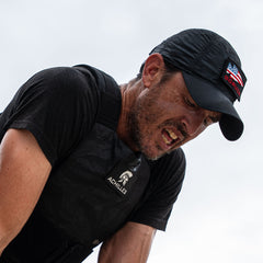 A man wearing the Achilles | Men's Weighted Vest and a black cap is pushing himself during intense outdoor exercise.