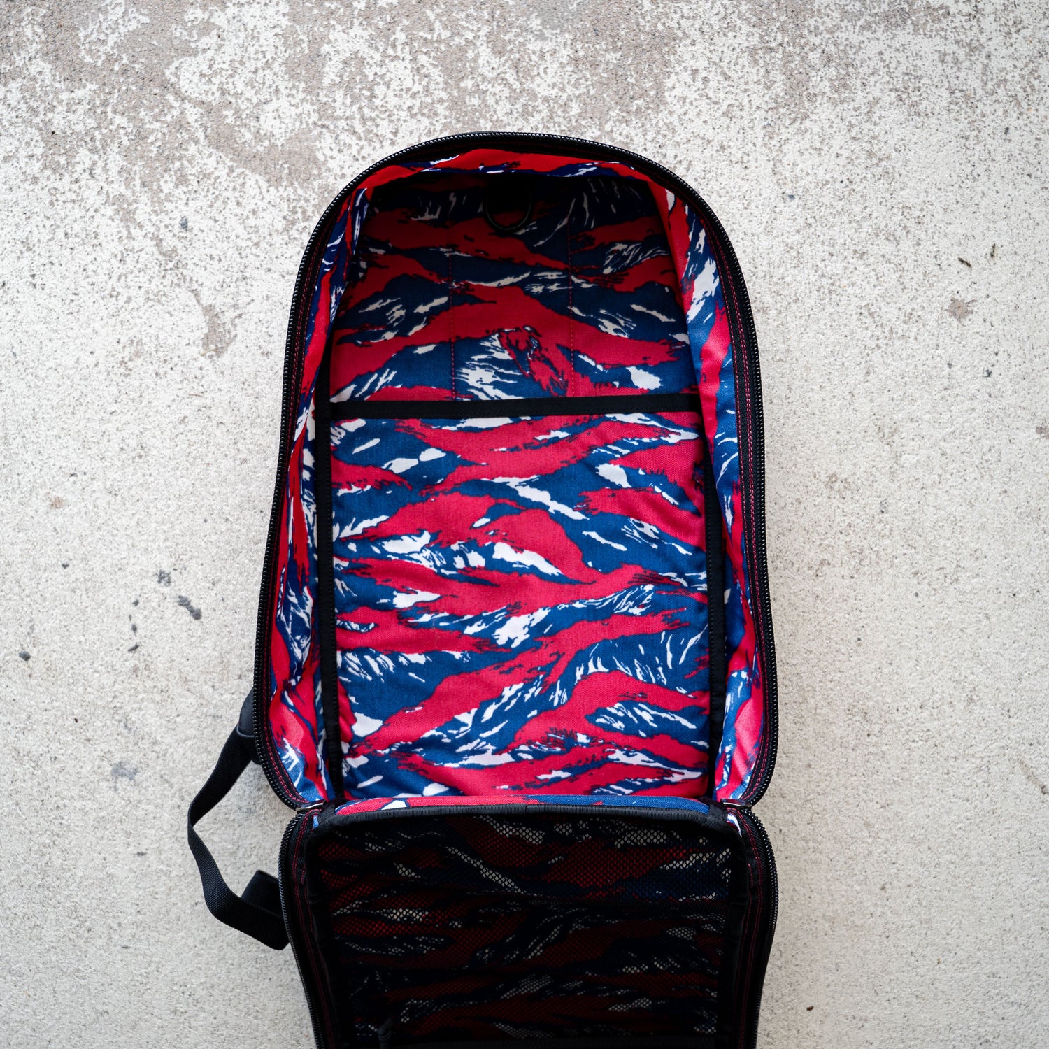 The Bullet Ruck Classic - Ballistic Nylon Cordura is open, revealing its red, blue, and white patterned lining as it lies on a concrete surface.