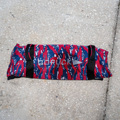 A Simple Training Sandbag with a red, blue, and white camo pattern rests on concrete, ideal for enhancing your home gym or sandbag workout routine.