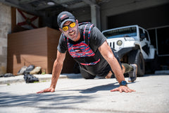 A man elevates his outdoor workout on a sunny day by doing push-ups near a white Jeep, wearing the Rucking Weight Vest.