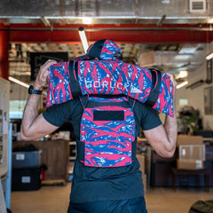 A person indoors wears a colorful life jacket labeled "SURFLEX" while standing beside Simple Training Sandbags, ready for a home gym workout.