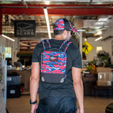 A man wearing the Ruck Plate Carrier 3.0 in red, white, and blue camo with ergonomic lumbar support and a matching cap stands inside a gear store.