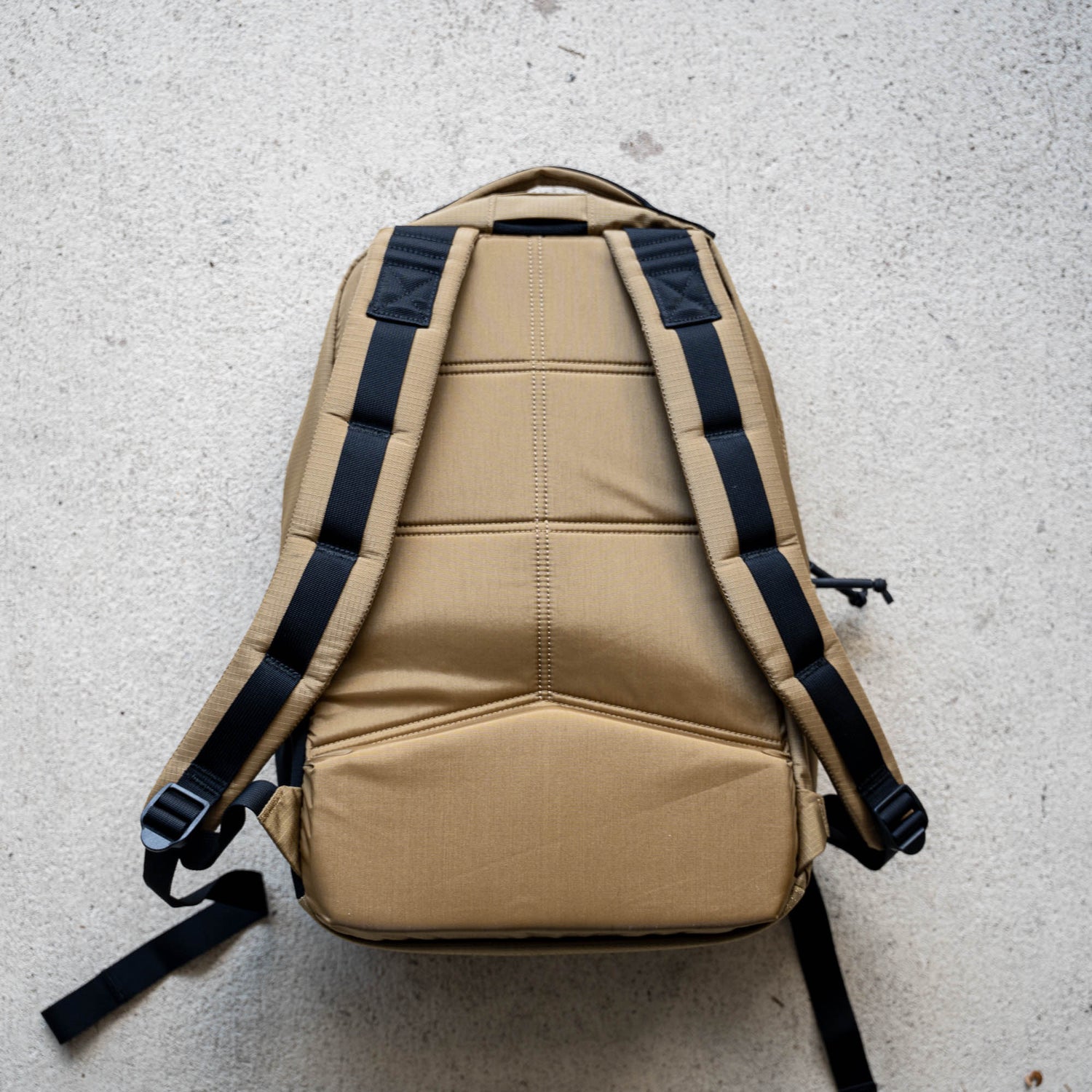 The Basic Rucker in tan with black straps is shown lying flat on a light-colored textured surface—an ideal choice for rucking with your favorite ruck plate.
