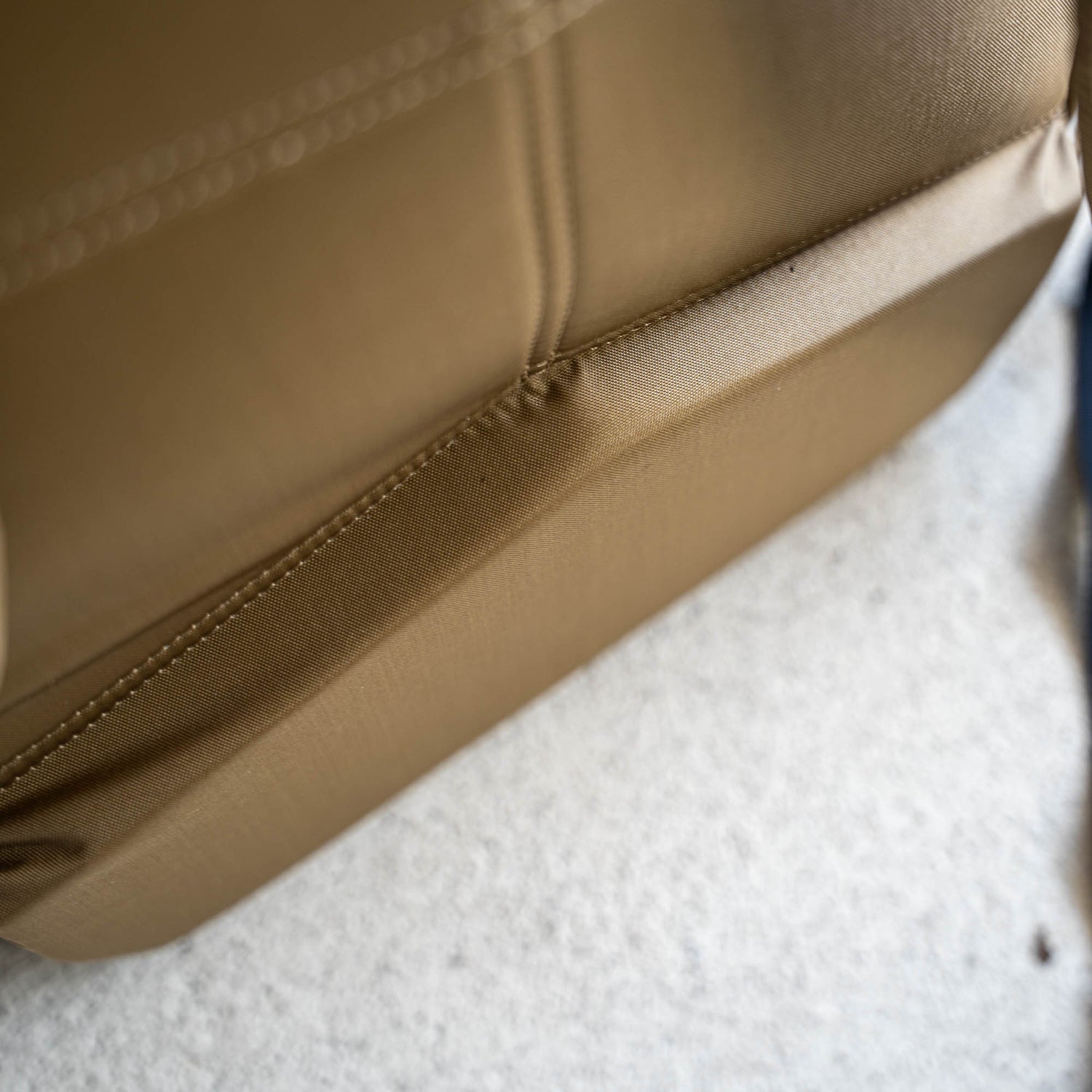 Close-up of a tan Basic Rucker resting on a light-colored, textured surface—ideal for carrying your ruck plate on any rucking adventure.