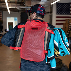 A man with a Mesh Ruck in red and a colorful towel over his shoulder stands indoors near an American flag.