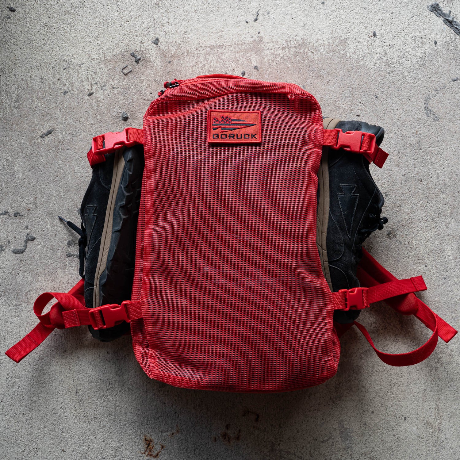 A red Mesh Ruck with black straps lies flat on a textured concrete surface.