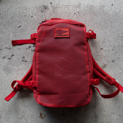 A red Mesh Ruck backpack featuring a "GORUCK" patch rests on a rough gray concrete surface.