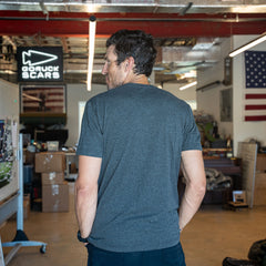 A man wearing the Slick Short Sleeve Tee - Tri-BlendX in gray stands with his hands in his pockets, facing away in an industrial office space.