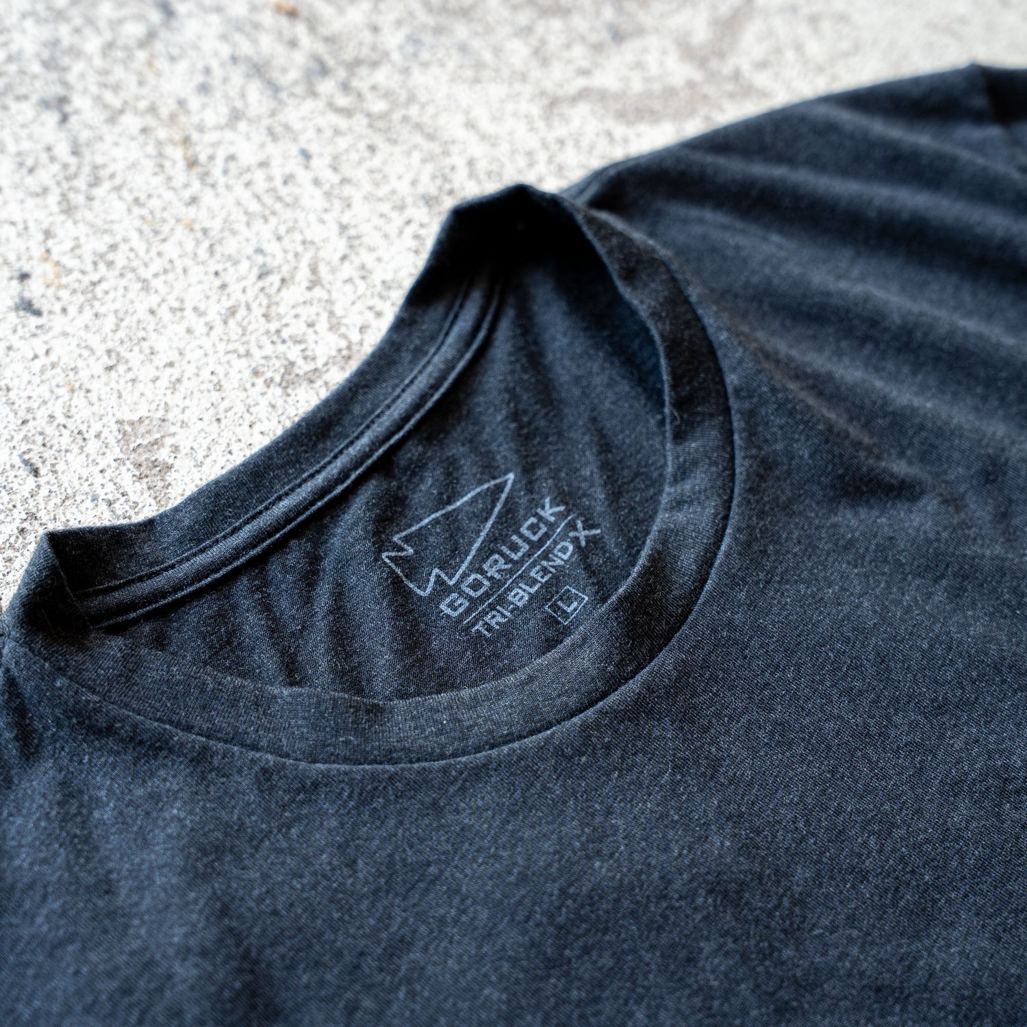 Close-up of the black Slick Short Sleeve Tee - Tri-BlendX collar with a printed label displaying the 
