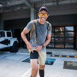 A smiling man in sunglasses and a cap stands outside near a white Jeep, pointing to his black Men’s Training Shorts - ToughStretch.