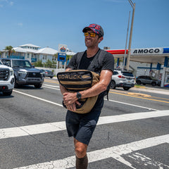 A smiling man in athletic wear crosses the street near an Amoco gas station, carrying Sand Tombstones—perfect for loaded carries.