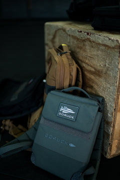 An RPC 3.0 + 10lb Ruck Sandplate sits beside a brown bag against a worn wooden box in a gym setting.