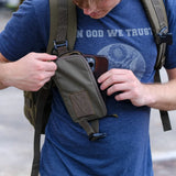 Man wearing GORUCK backpack opening green utility pouch on shoulder strap outdoors