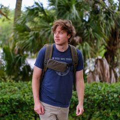Young man wearing GORUCK backpack and chest pouch outdoors with tropical greenery background