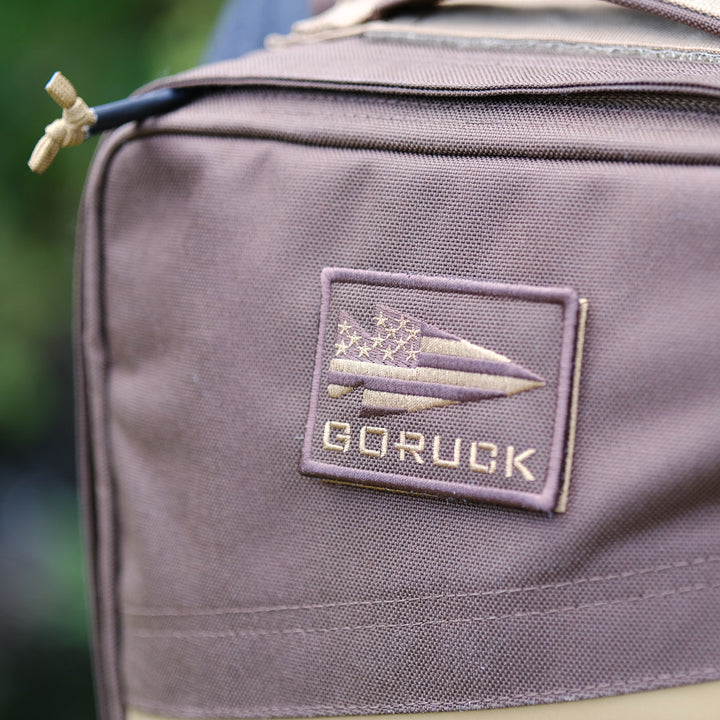 Close-up of a brown Rucker 4.0 rucksack with a patch featuring an arrow and stars on the front—ideal for rucking or carrying your ruck plates in style.