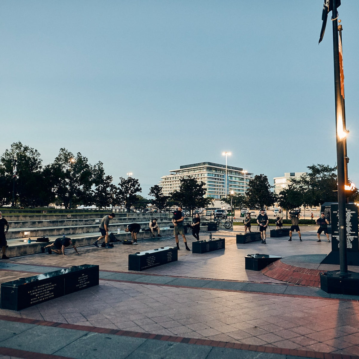 A group of people performing a rucking challenge in a public plaza at dusk.