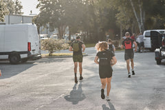 People jogging outdoors on a sunny day, wearing the RPC 3.0 + 10lb Ruck Sandplate for weighted training, with cars and trees in the background.