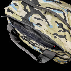 A camouflage "Kit Bag (Includes Shoulder Strap)" by GORUCK, showcasing black, beige, and blue patterns reminiscent of an Aviator’s Kit Bag. The open top reveals a black mesh pocket inside. It also features black handles and a partially open zipper against a black background.