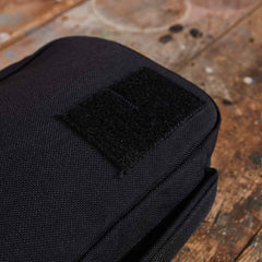 A close-up of the GR1 Field Pocket - USA, a black fabric pouch with a Velcro patch, perfect as an electronics organizer, shown on a worn wooden surface.