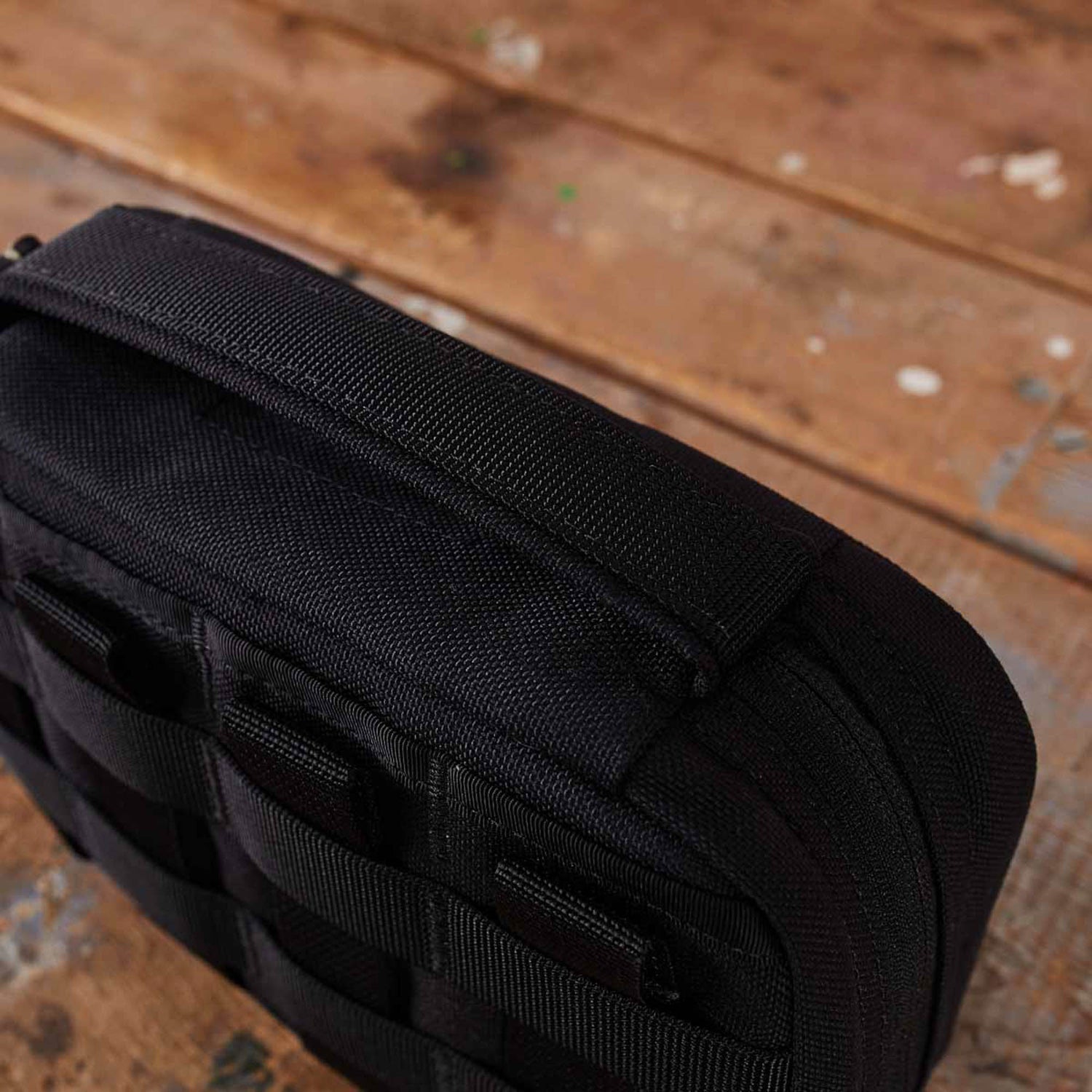 Close-up of the GR1 Field Pocket - USA, a black tactical bag with webbing, perfect as an electronics organizer, resting on a scratched wooden surface.