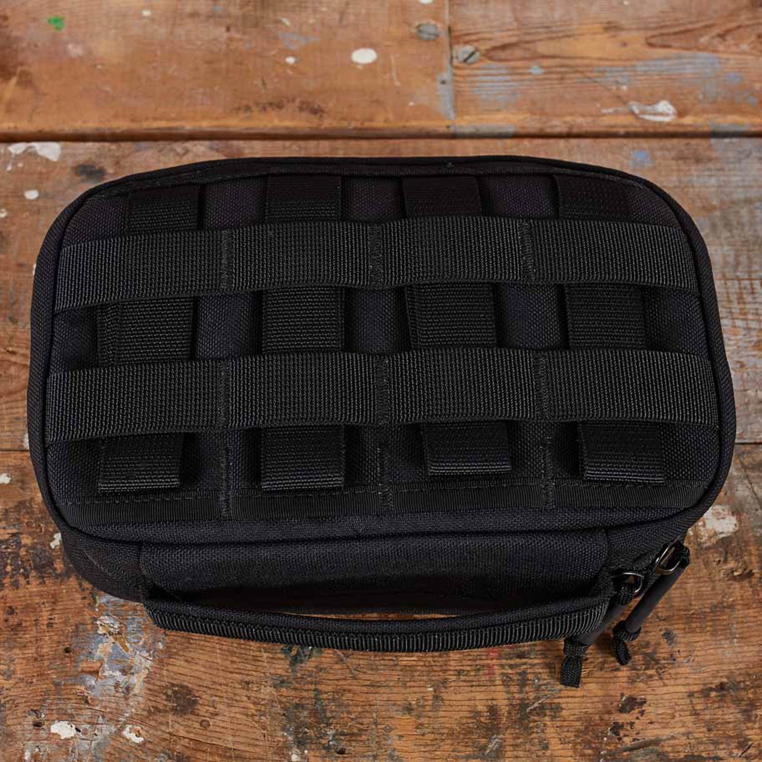 The GR1 Field Pocket - USA, a black tactical pouch ideal for organizing electronics or camera gear, rests on a worn wooden surface.