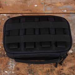 The GR1 Field Pocket - USA, a black tactical pouch ideal for organizing electronics or camera gear, rests on a worn wooden surface.