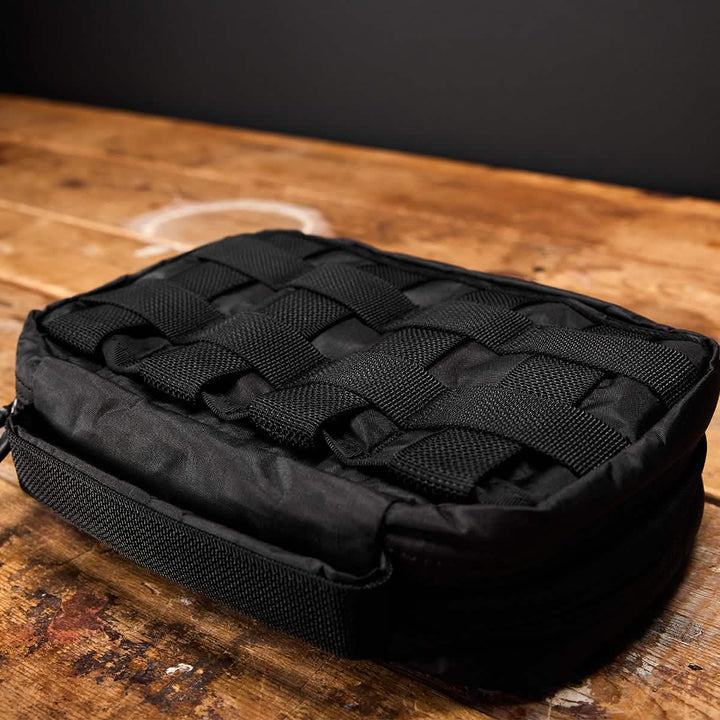 The GR1 Field Pocket - Dyneema by GORUCK, in a sleek black design, features a grid of straps on top and is set on a wooden surface. This rectangular travel accessory is crafted for durability, making it ideal for versatile storage or outdoor use.