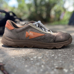 The Mackall 45 Fog sneaker, featuring brown and orange accents, rests on a rough concrete surface outdoors.
