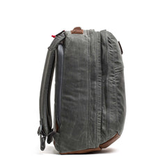 Side view of the GR2 - Heritage Waxed Canvas backpack in green with brown Red Wing Leather accents and padded shoulder straps, standing upright.