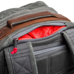 Close-up of the GR2 - Heritage Waxed Canvas backpack in gray and brown, showing a red lining through a partially open zipper pocket.