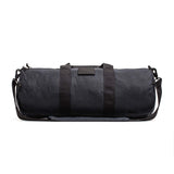 The Gym Bag - Waxed Canvas features classic black waxed canvas, two handles, a shoulder strap, and a minimalist design, all set against a white background.