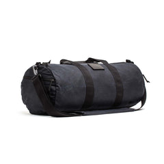 The Gym Bag - Waxed Canvas features handles and an adjustable shoulder strap, made from durable black waxed canvas and shown against a white background.