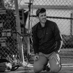 A man kneels by a chain-link fence, looking distressed in black and white—an image that truly embodies the spirit of the Patch - Embrace The Suck.