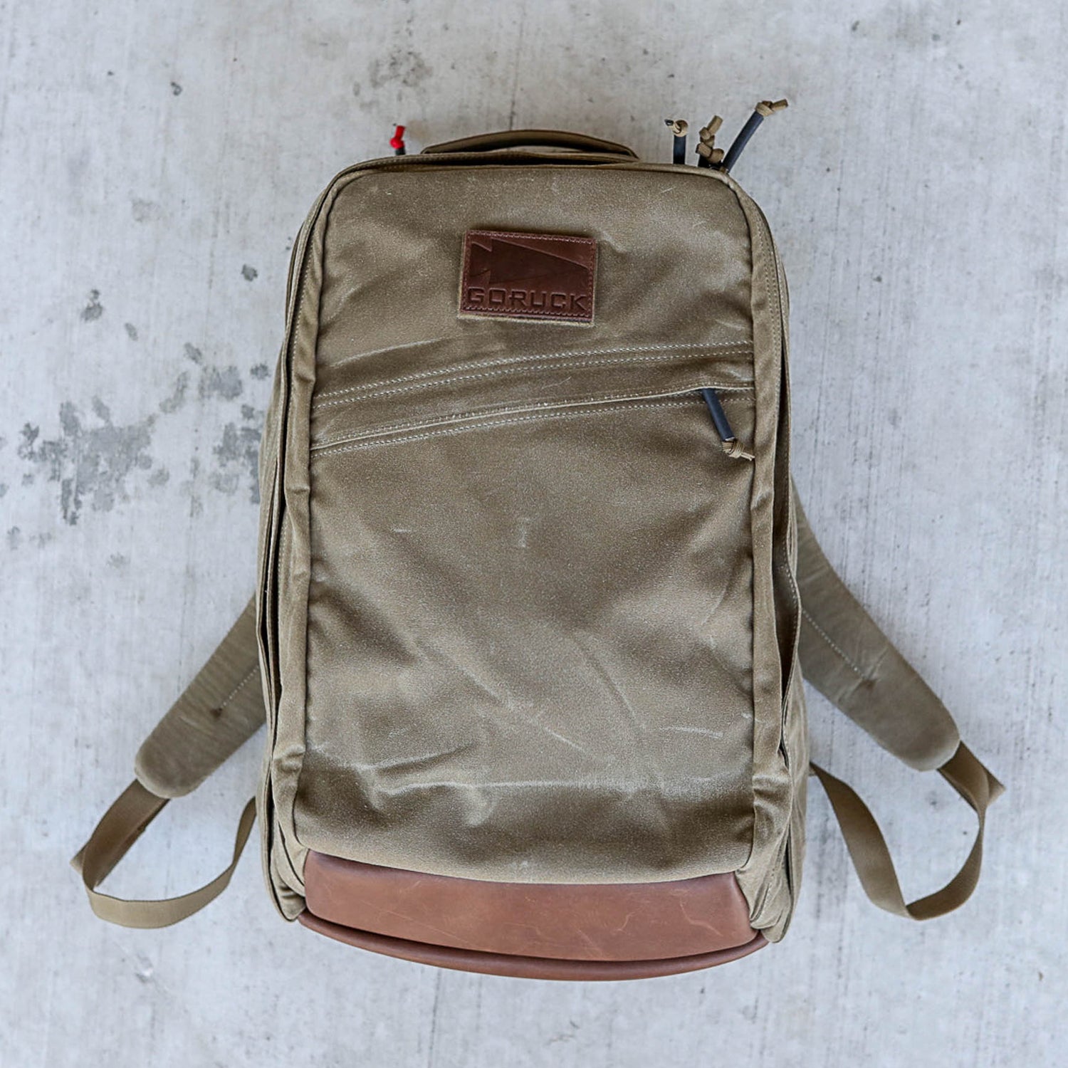 A khaki GR2 - Heritage Waxed Canvas ruck with leather accents and a Martexin wax finish rests on a concrete surface.